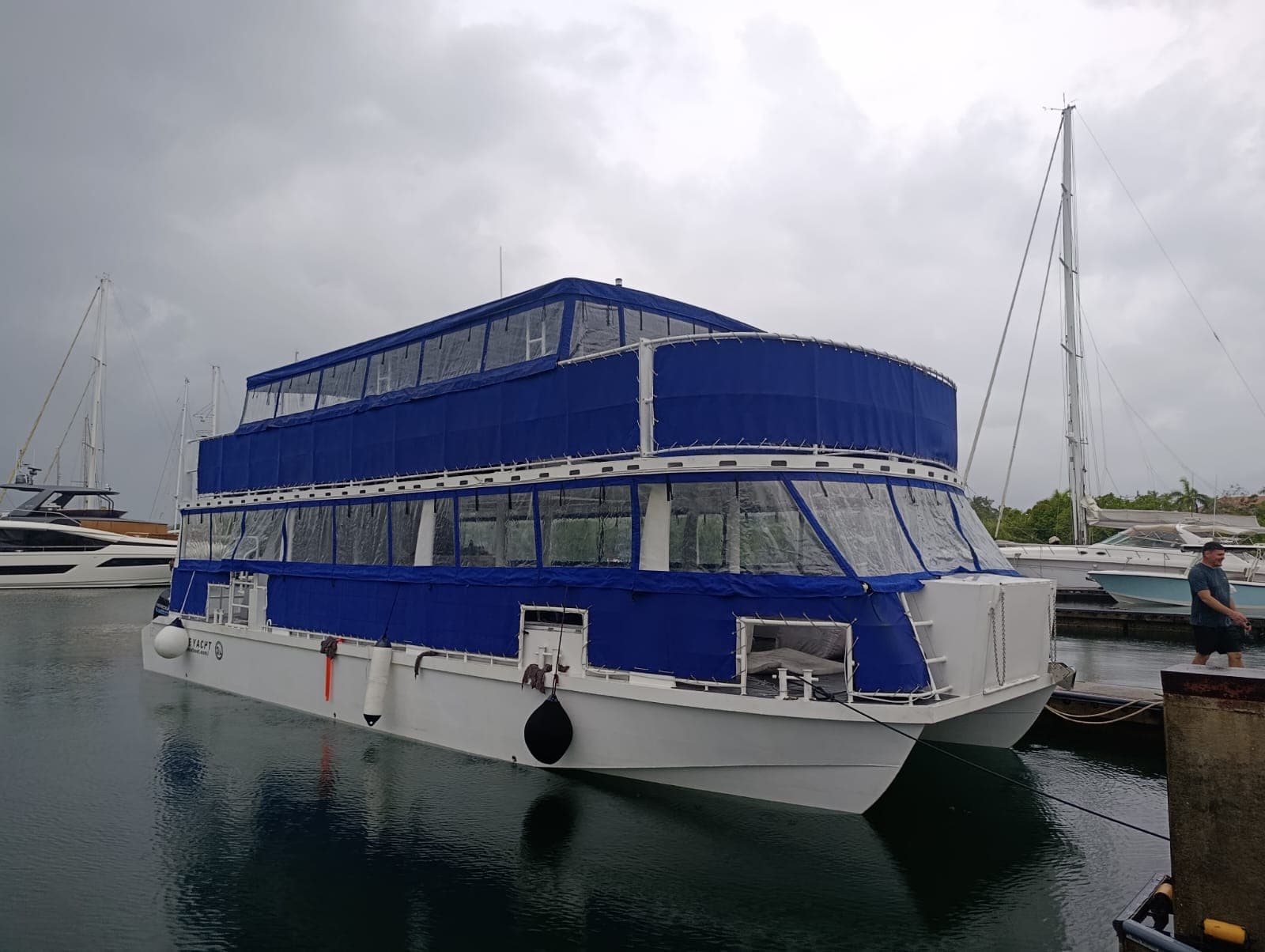 Catamarán Sirena del Mar atracado en la marina, de dos pisos y con lona azul